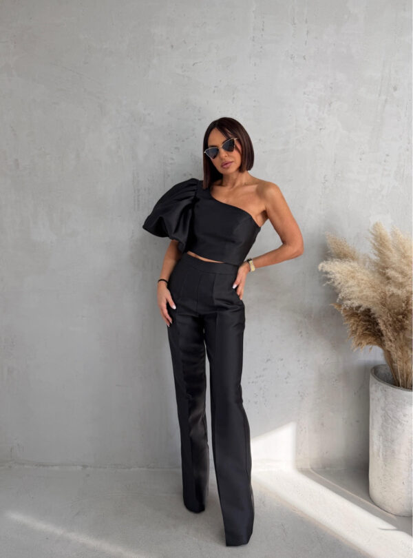 Crni komplet od čvrstog punijeg satena koji se sastoji od zvonastih pantalona visokog struka i kropovane asimetrične bluze sa predimenzioniranim rukavom