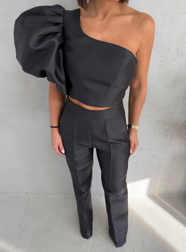 Crni komplet od čvrstog punijeg satena koji se sastoji od zvonastih pantalona visokog struka i kropovane asimetrične bluze sa predimenzioniranim rukavom