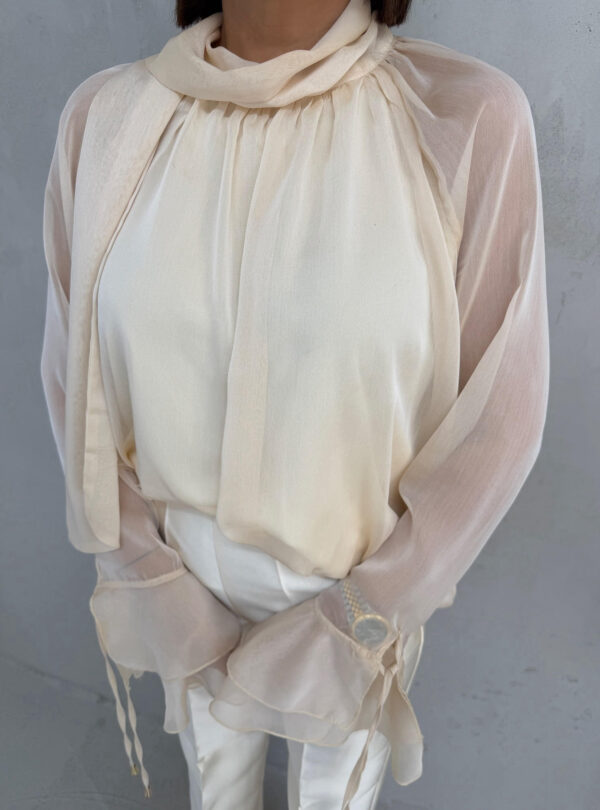Bež lepršava polu-transparentna bluza sa karnerima na krajevima rukava i dekorativnim vezivanjem oko vrata