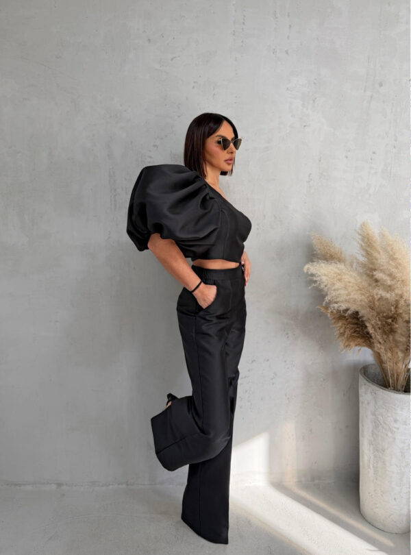 Crni komplet od čvrstog punijeg satena koji se sastoji od zvonastih pantalona visokog struka i kropovane asimetrične bluze sa predimenzioniranim rukavom