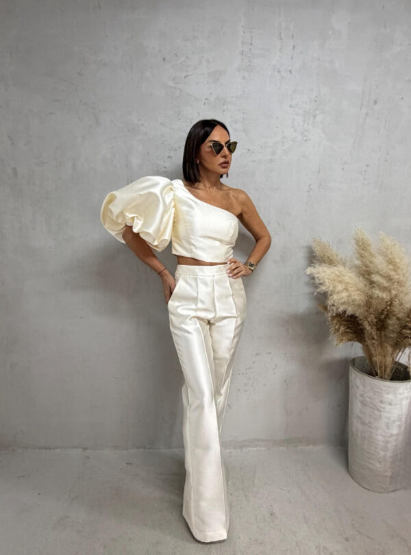 Bež sjajni komplet od čvrstog punijeg satena koji se sastoji od zvonastih pantalona visokog struka i kropovane asimetrične bluze sa predimenzioniranim rukavom